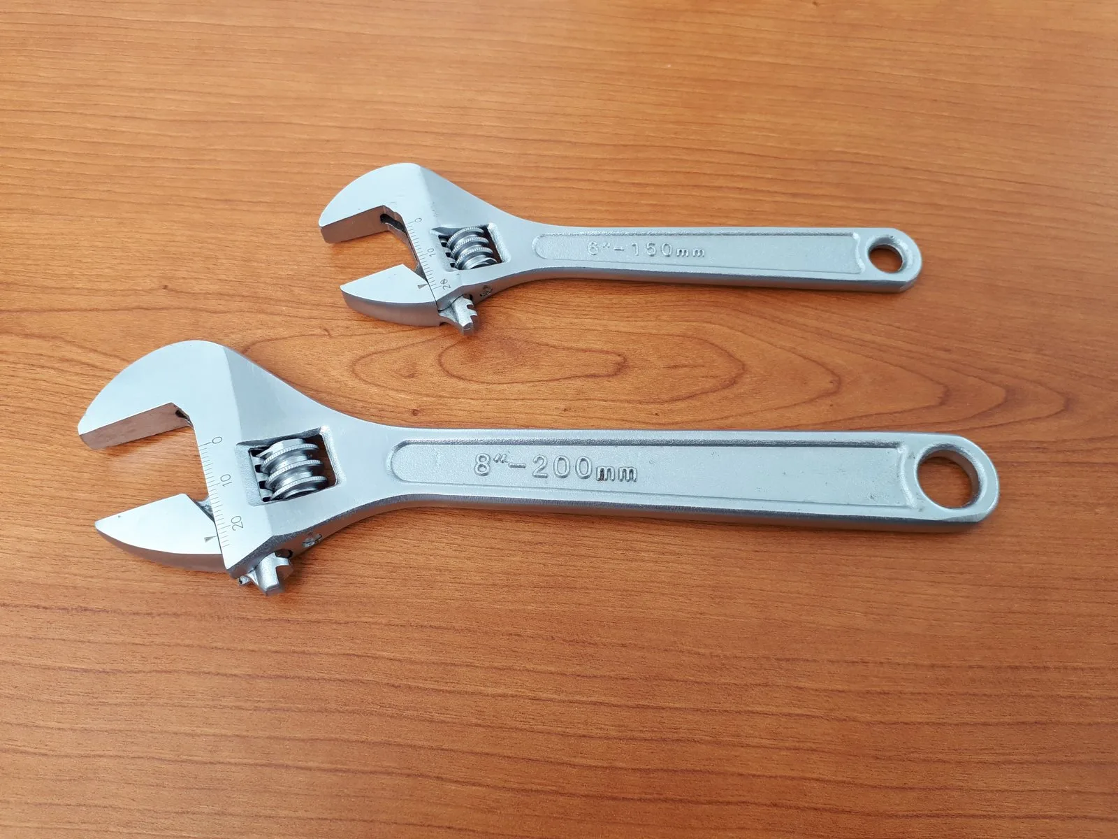 Two adjustable wrenches, one small and one large, on a wood workbench